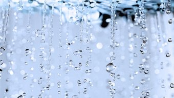 Wassertropfen fallen in einer sanften Bewegung, während sie im Licht funkeln und eine ruhige Atmosphäre schaffen.