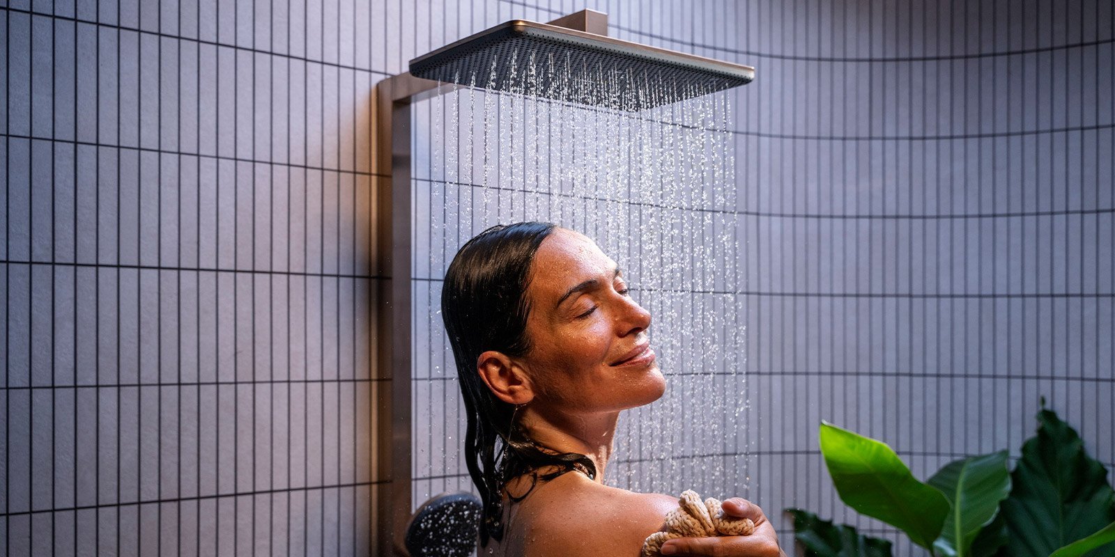 Eine Frau genießt eine erfrischende Dusche, während Wasser sanft über ihr Gesicht fließt und sie entspannt lächelt.