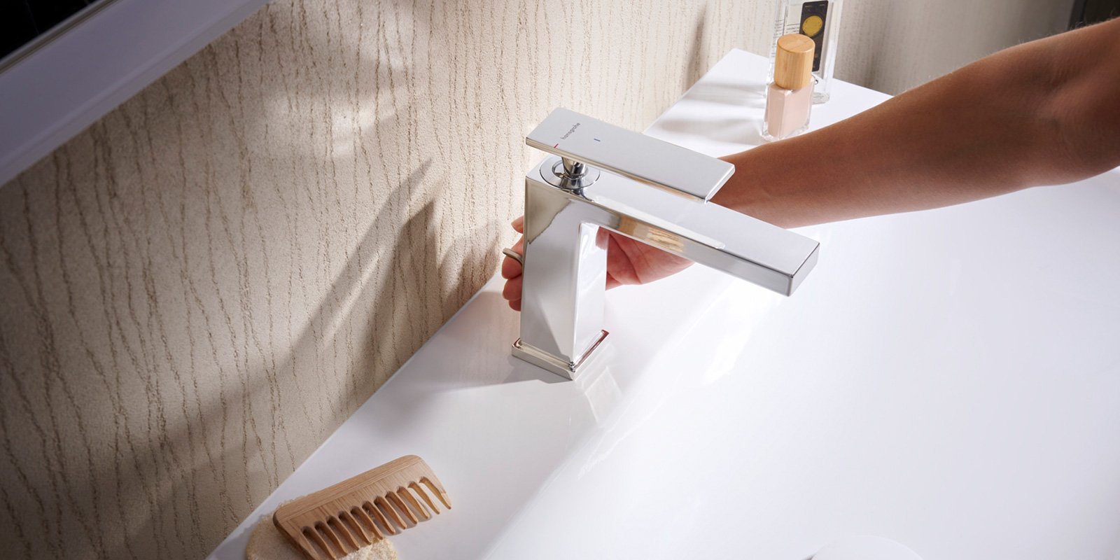 Eine Hand dreht den Wasserhahn in einem modernen Badezimmer, während ein sanftes Licht auf die glänzende Oberfläche fällt.