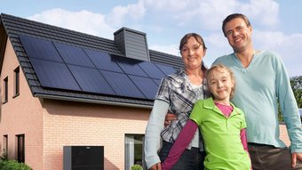 Eine kleine Familie, im Hintergrund ist ein Haus mit einer Photovoltaikanlage